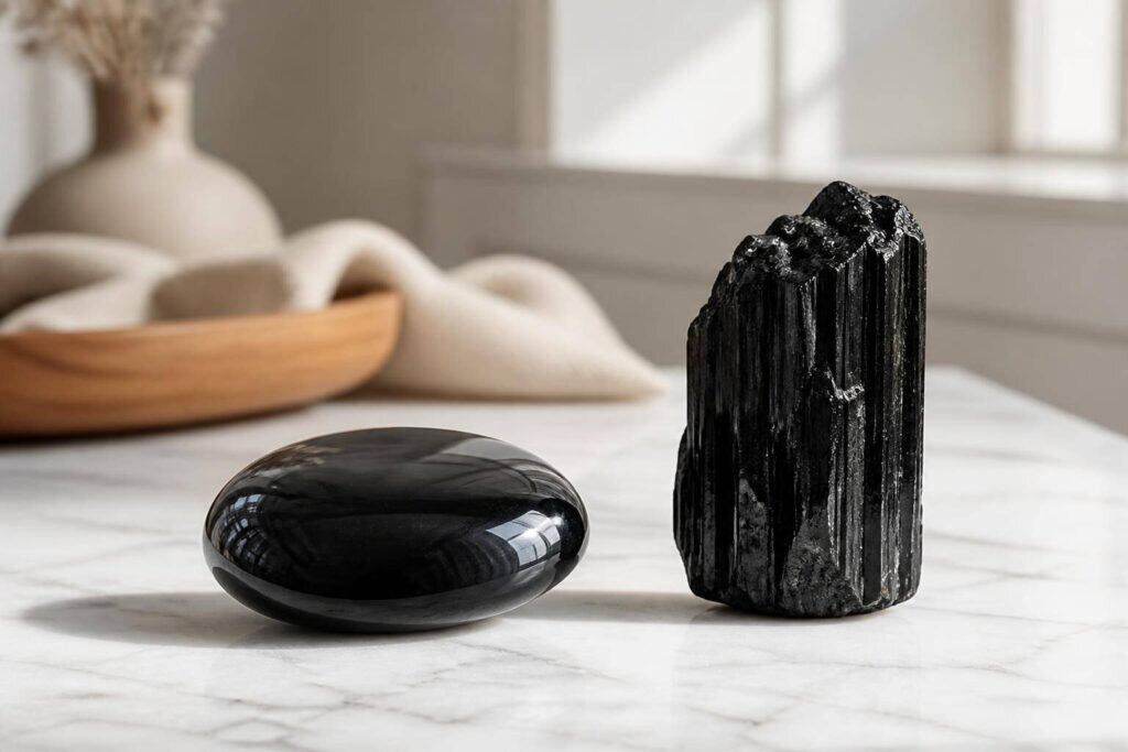 Photographie haut de gamme de deux pierres noires distinctes, une obsidienne polie et un cristal de tourmaline brute, sur une surface en marbre blanc mat.